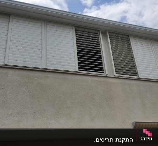 תריסים לבנים סגורים וחלקם פתוחים בחלון עליון